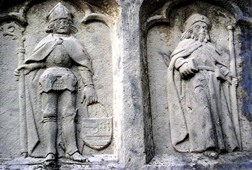 St. Arnoldus in wapenuitrusting en met de bisschopsattributen (l.) en St. Jakob van Compostela (r.). Witstenen beeldhouwwerk, 15de eeuw. Oudenburg, archeologisch museum